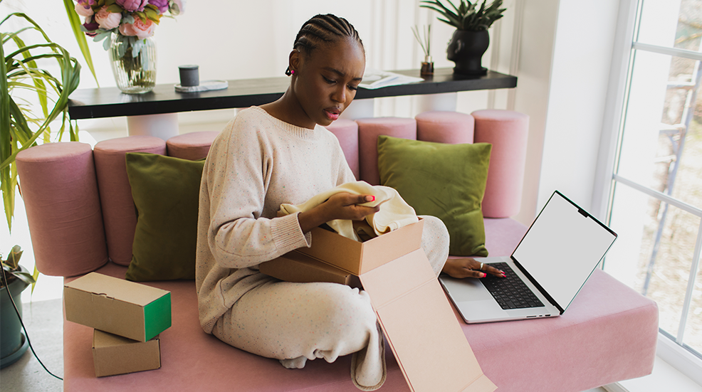 Black woman opening a box with her online order, with a laptop open beside her